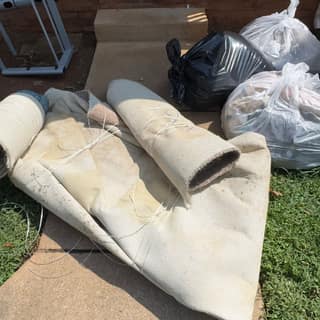 Rolled-up carpet and bagged trash on a lawn awaiting pickup